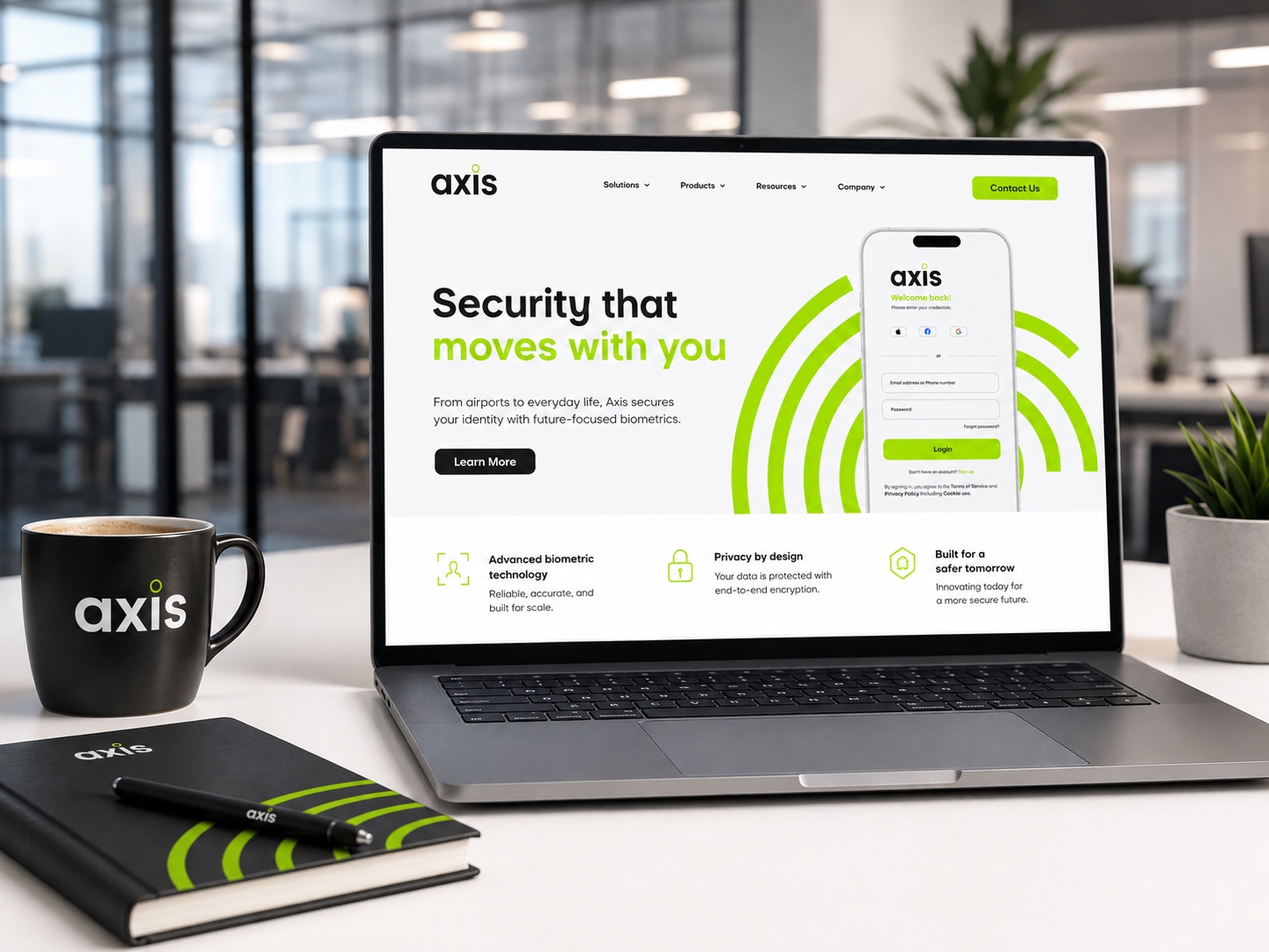 Axis website homepage on a table, with a coffee mug and branded note book and pen.
